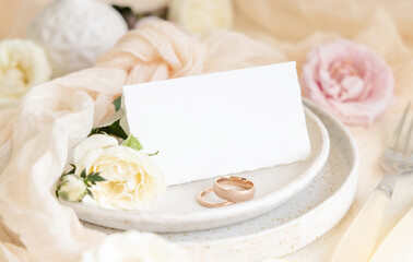 Folded Card near light pink fabric and cream flowers on plate close up, copy space, wedding mockup