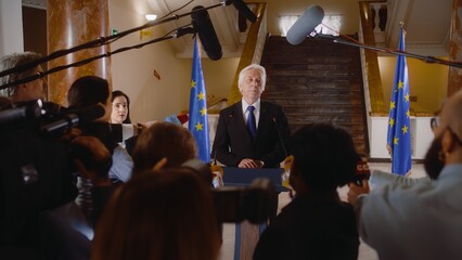 Senior EU representative comes to press conference and gives interview for TV breaking news in government building hall. Consul surrounded by journalists crowd. Political speech. Hot button issues. - obrazy, fototapety, plakaty