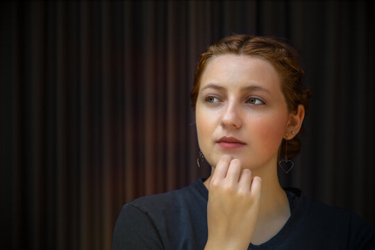 pensive young woman thinking hand on chin on dark background