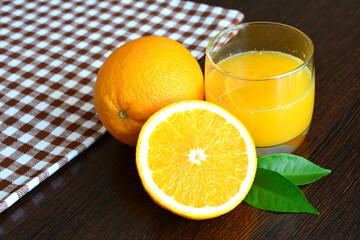 a glass of orange juice next to two oranges on checkered towel