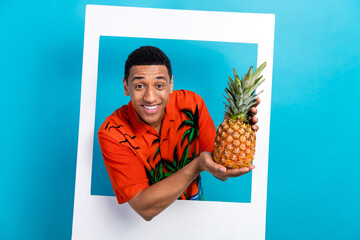 Photo of cool excited guy dressed print shirt holding pineapple white photo frame isolated blue...