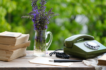 old books, rotary telephone, wild flowers on old wooden table in garden, remote work in summer in...