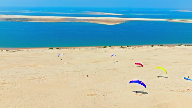 Panoramic view on the tallest sand dune in Europe, a Natural feature in France. Aerial view of tourists enjoying paragliding at the famous Dune of Pilat alongside the shore in France.