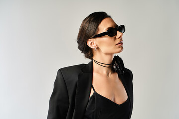 A stylish and mysterious woman dons a sleek black suit and trendy sunglasses in a studio against a...