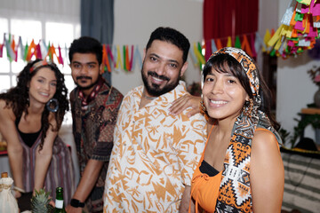 Obraz premium Happy young Hispanic couple in ethnic apparel looking at camera against their friends bending over served festive table in living room
