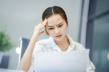 Fototapeta premium Asian people, In the corporate office, a young businesswoman sits at her desk, feeling exhausted and frustrated. facing financial crisis, overworked and stressed, hoping for a successful outcome.