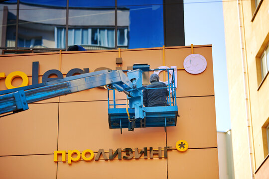 Minsk, Belarus. Mar 2, 2024. Worker in crane bucket installing outdoor advertising on building facade. Man on cherry picker installs luminous advertising words PROleasing. Man work on aerial platform