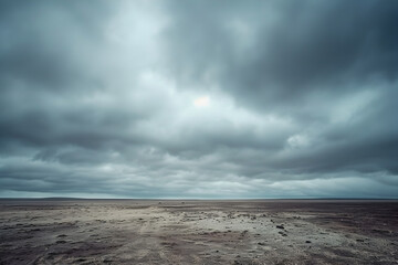 Dramatic landscape with overcast sky, featuring expansive barren fields leading to a distant horizon, conveying a sense of desolation and vastness.