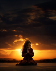 Prayer concept. Silhouette of a young child girl in a praying pose. Set against a vibrant sunset sunrise sky. Clasped hands. Also ties in with presence, renewal, connection, journey, gratitude, relax