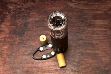 An electric corkscrew and wine bottle caps lie on a dark wood table, preparing for holiday.