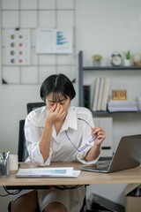 Exhausted female office worker feeling stressed, holding glasses, with laptop and documents on desk.