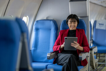 Smiling businesswoman in a yellow blazer using a laptop on a tray table, working efficiently on an...