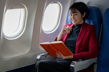 Smiling woman sitting by the airplane window, engrossed in writing notes in her orange notebook.