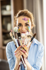 Portrait of a cute Latin woman holding a bunch of paintbrushes with both hands and smiling - 782160463