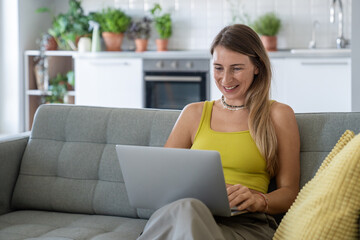 Happy woman sitting with laptop on lap on sofa receive interesting good news. Satisfied cheerful female with portable computer on knees chatting in social media, online shopping, have fun in internet.