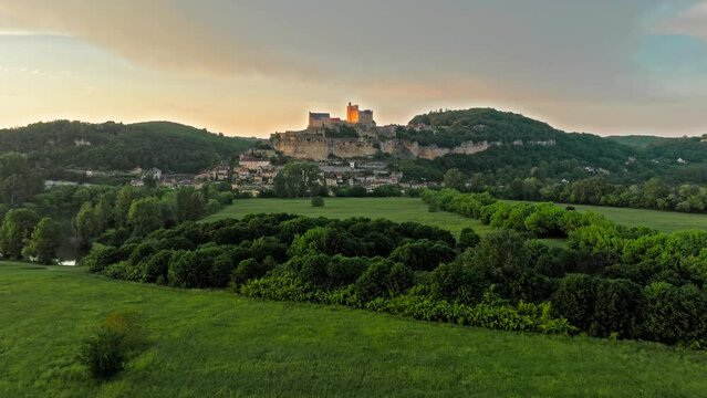 Cinematic panoramic view of feudal square-shaped castle on a riverside clifftop at golden sunset in France. Aerial view of a Hulking medieval fortress with a Romanesque keep and a frescoed chapel.
