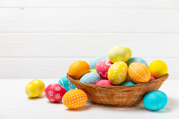 Easter basket filled with colorful eggs and a bouquet of tulips on a textured wooden table. Easter celebration concept. Colorful easter handmade decorated Easter eggs. Place for text. Copy space