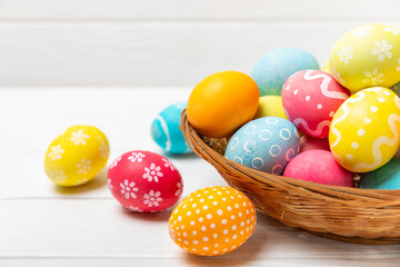 Easter basket filled with colorful eggs and a bouquet of tulips on a textured wooden table. Easter celebration concept. Colorful easter handmade decorated Easter eggs. Place for text. Copy space