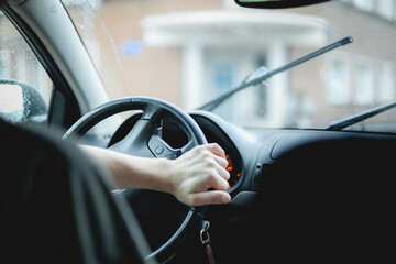 Naklejka premium A young caucasian guy keeps his hand on the steering wheel while turning a car driving on a rainy day