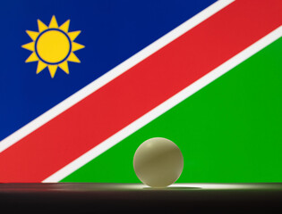 Obraz premium The table tennis ball stands on a surface in front of Namibia flag.