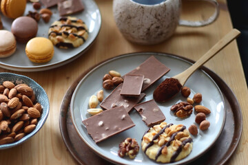 Cup of tea or coffee, cookies, macaroons, chocolate, various nuts and cocoa powder on wooden table. Selective focus.