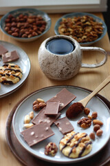 Cup of tea or coffee, cookies, macaroons, chocolate, various nuts and cocoa powder on wooden table. Selective focus.