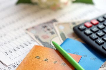 Japanese pension insurance booklets on table with yen money bills and calculator on table close up