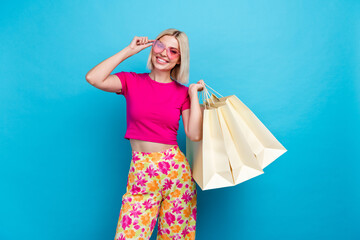 Photo portrait of attractive young woman sunglass hold shopping bags dressed stylish pink clothes isolated on blue color background.