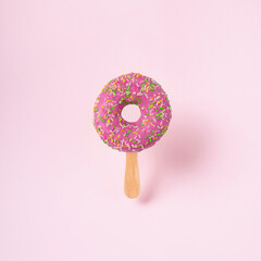 Pink glazed donut with ice cream stick on pink pastel background. Creative food concept.