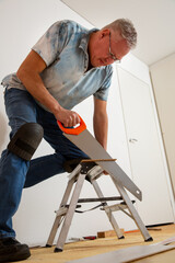 Two mature men installing laminate flooring in a new home together. DIY concept. Professional...