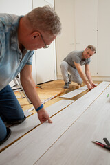 Two mature men installing laminate flooring in a new home together. DIY concept. Professional renovation of a house.