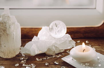 Gemstone sphere or crystal ball on quartz geode on wood tray, candle burning. Tranquil home concept.