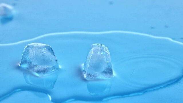 Two ice cubes melting in clear glass filled with water. Crystal-clear droplets. Refreshment and coolness. Concept of refreshment, aesthetics of product, health, wellness, hydration