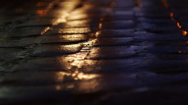 Macro photography of paving stones on the road at night during the rain. The color of the headlights of passing cars constantly changes.