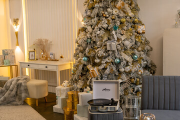 A Christmas tree with a record player on top of it. The room is decorated with presents and a white desk with a picture on it.