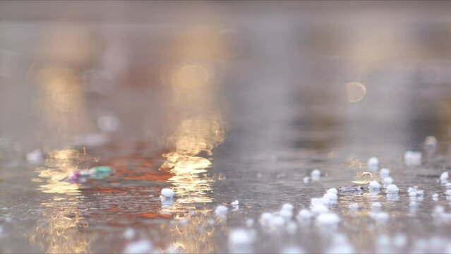 A city road is flooded with water after a hail storm. Yellow light is reflected in the water, the background is blurred.