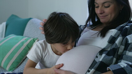 Boy's Loving Kiss to Unborn Brother, Tender Moment with Pregnant Mother on Home Couch. Third...