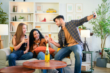 Friends capturing a joyful selfie moment with champagne, sharing laughter in a vibrant, homey living room.