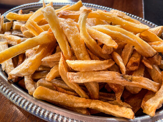 A pile of golden french fries on a decorative silver platter