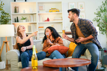 Group of happy friends laughing and toasting with glasses of champagne in a cozy, sunlit living room at home.