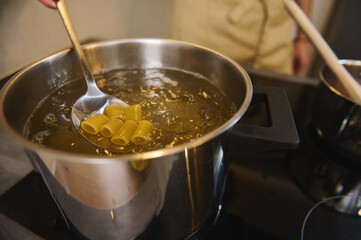 Close-up mixing Italian pasta in a boiling water, preparing spaghetti to the condition Al Dente. Chef cooking pasta, standing at electric stove or induction cooker. Extreme closeup