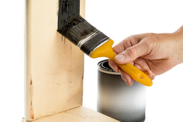close up of a man is painting a piece of wood with black paint using a yellow paint brush with a...