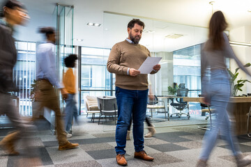 Businessman standing in the office. Other colleagues walking by.