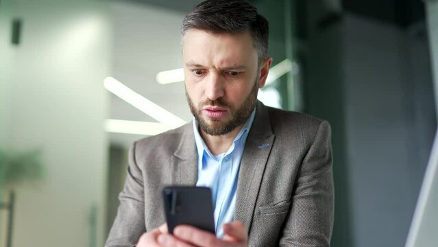 Frustrated stressed businessman having problems with software or service on phone sitting at workplace in business office. Worried angry man worker complains about a bad internet connection. Close up