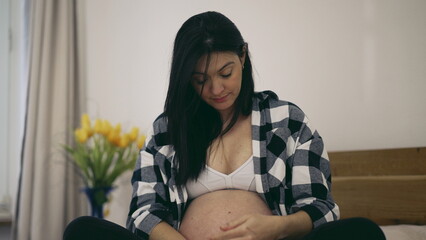 Third trimester pregnancy - woman caresses pregnant belly in 8 month expecting baby seated in bed...