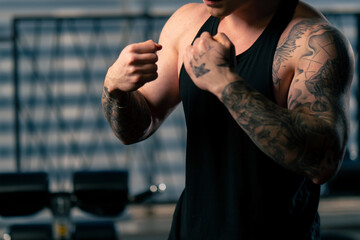 close up in the gym young handsome guy with tattoos in a black T-shirt is doing a warm-up in front...