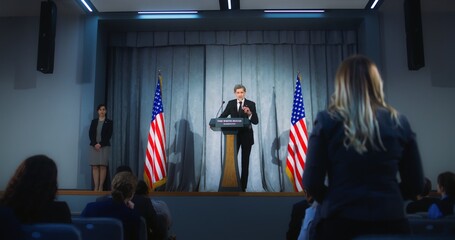 Confident American republican politician delivers successful speech to supporters at government election rally. New president of USA gives interview for media. Backdrop with American flags. Zoom out. - obrazy, fototapety, plakaty