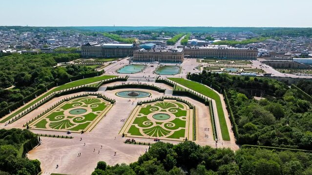 Aerial view of Immense French palace with gilded apartments, chandeliered Hall of Mirrors and fountain show. Fortress castle, Palace of Versailles drone aerial view with landscaped gardens in France.