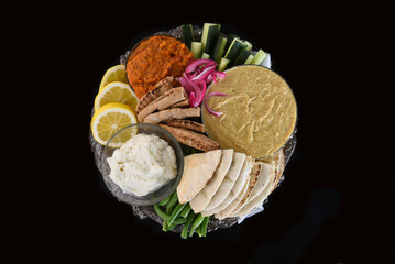 High angle shot of a bowl filled with hummus, and other dips, vegetables and pita bread.