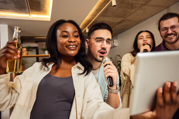 Multiracial group of friends having karaoke night. Singing in to the microphone, looking at lyrics...